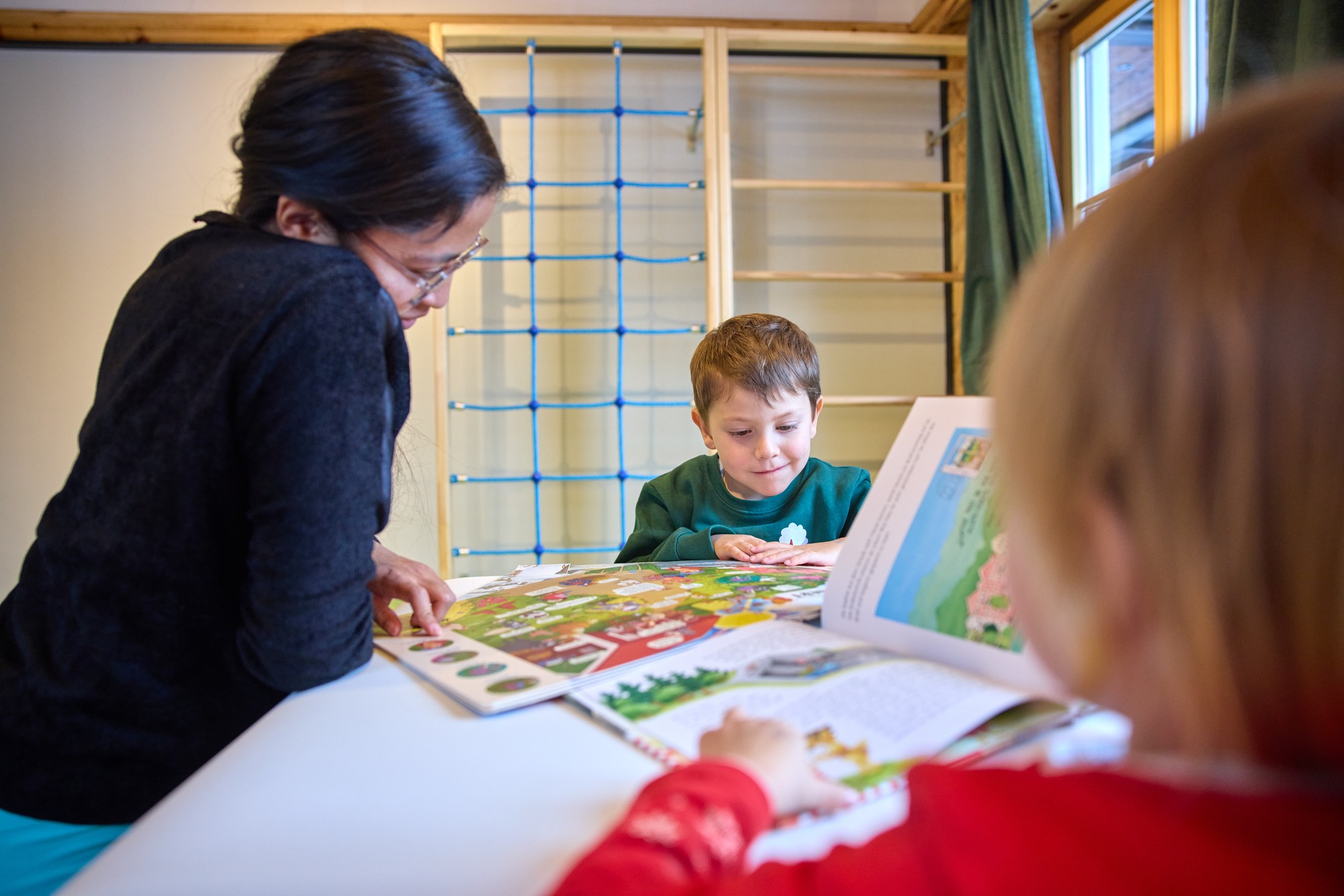 Kinder und Erwachsene lesen am Tisch vor dem Kletternetz