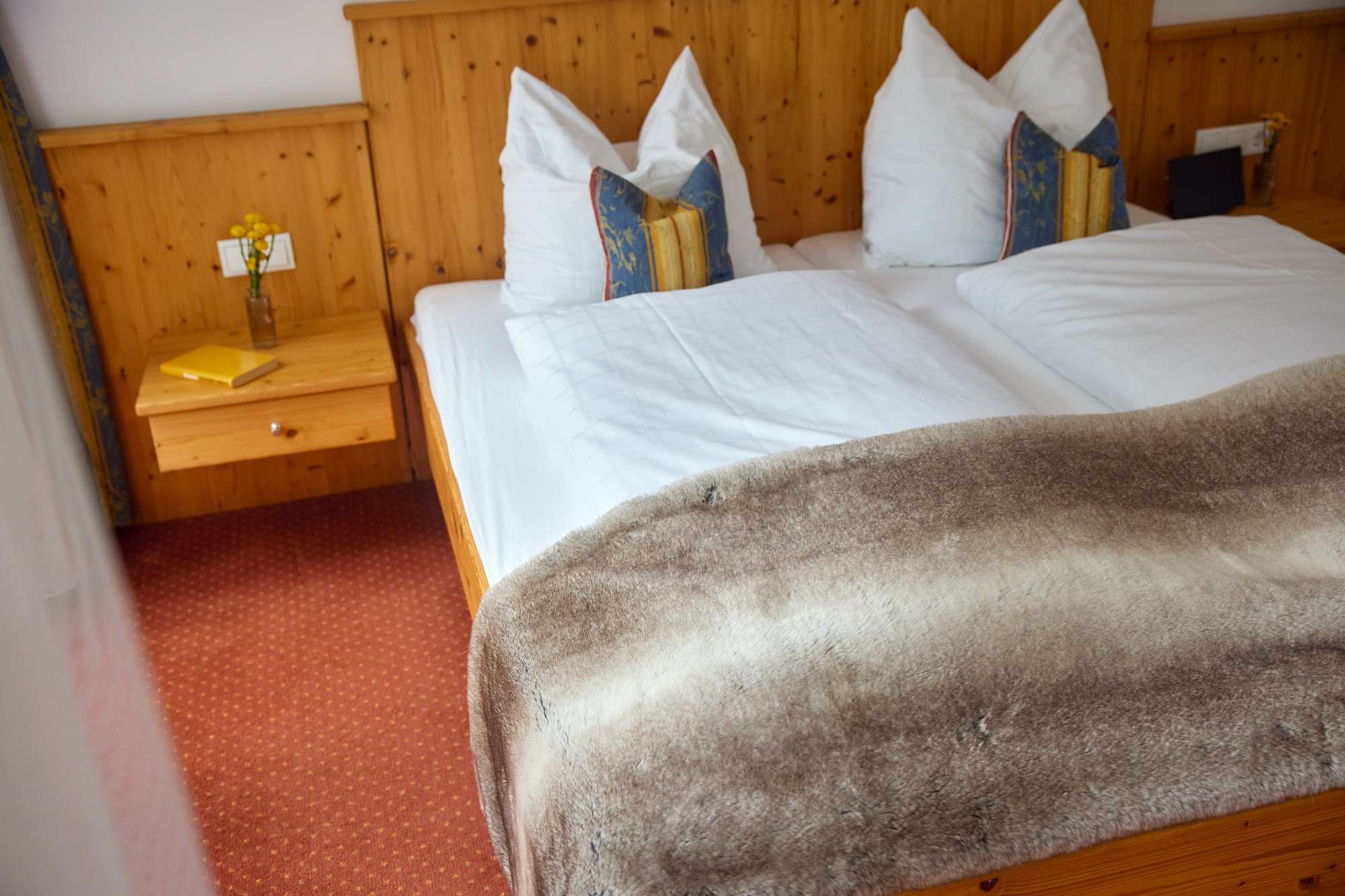 Holzbett mit weißer Bettwäsche und Felldecke im Doppelzimmer Plus
