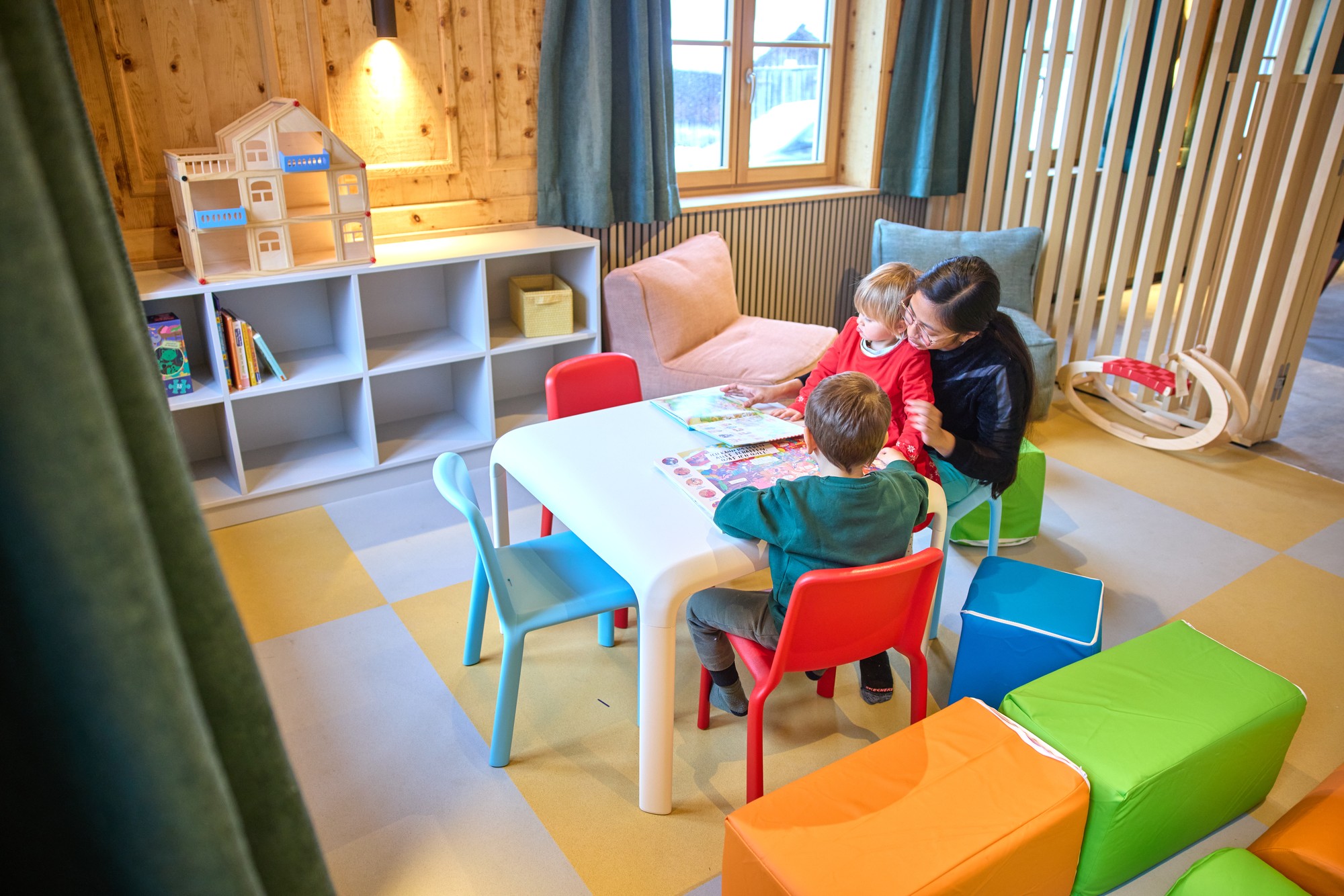 Kindertisch mit bunten Stühlen, Puppenhaus und Bilderbüchern im Kidsroom