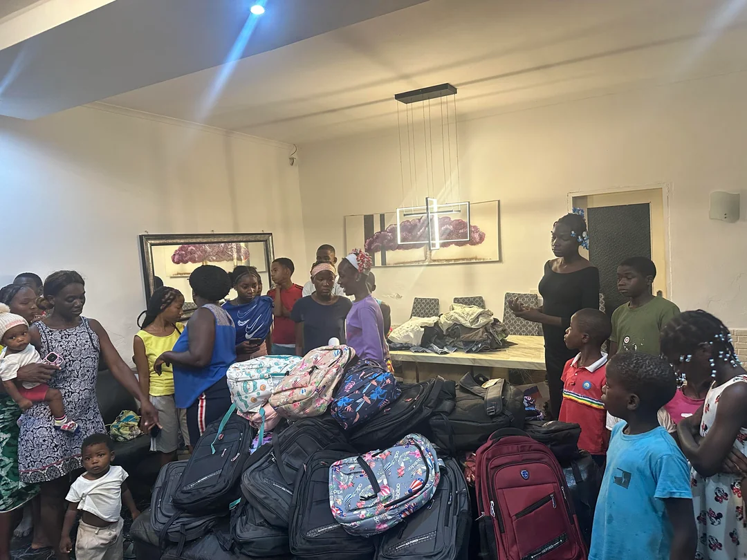 Uma sala cheia de famílias e crianças com mochilas escolares empilhadas para distribuição em São Tomé
