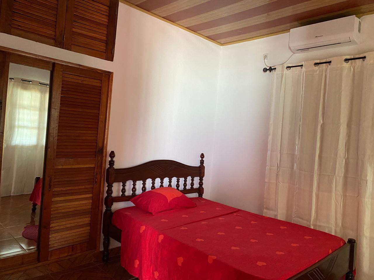 Quarto de casal com cama de madeira esculpida, roupa de cama vermelha e ar condicionado