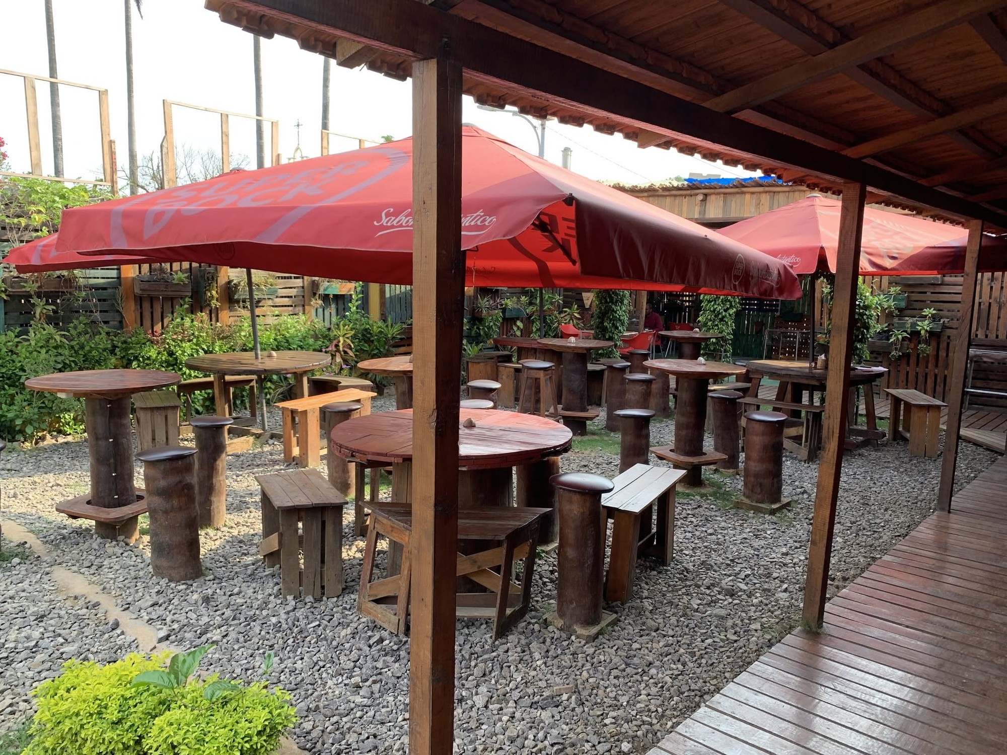 Outdoor seating at Zima bar in São Tomé, wooden barrel tables and stools under red Sagres umbrellas