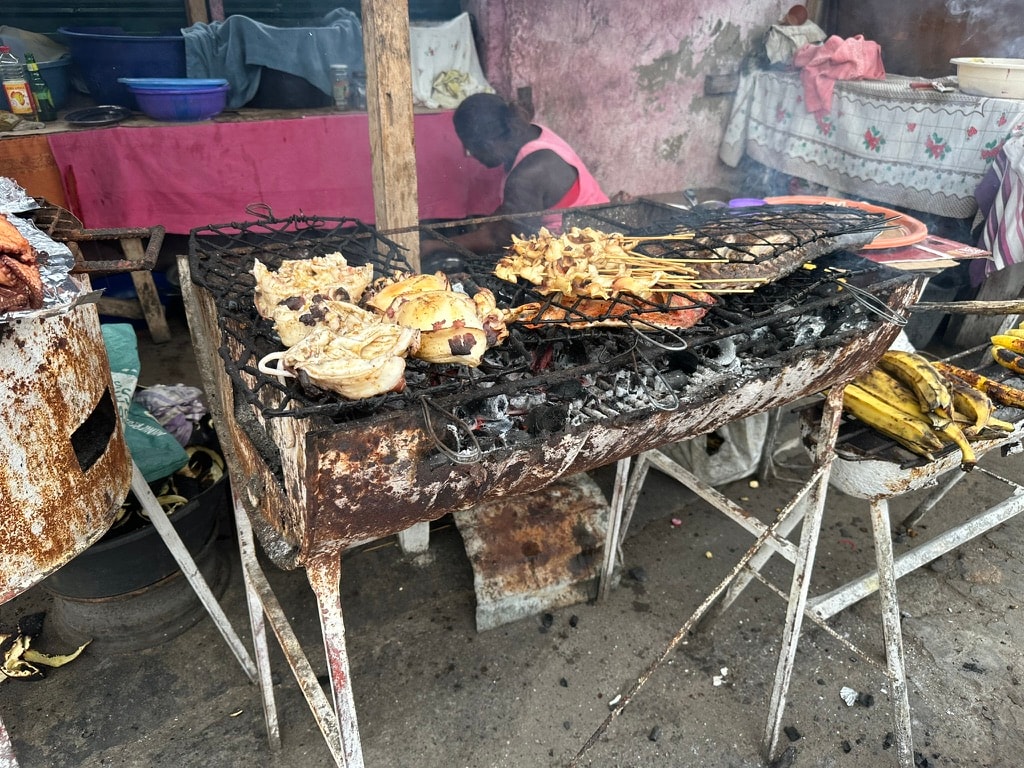 Street grill with chicken and skewers cooking over charcoal in São Tomé