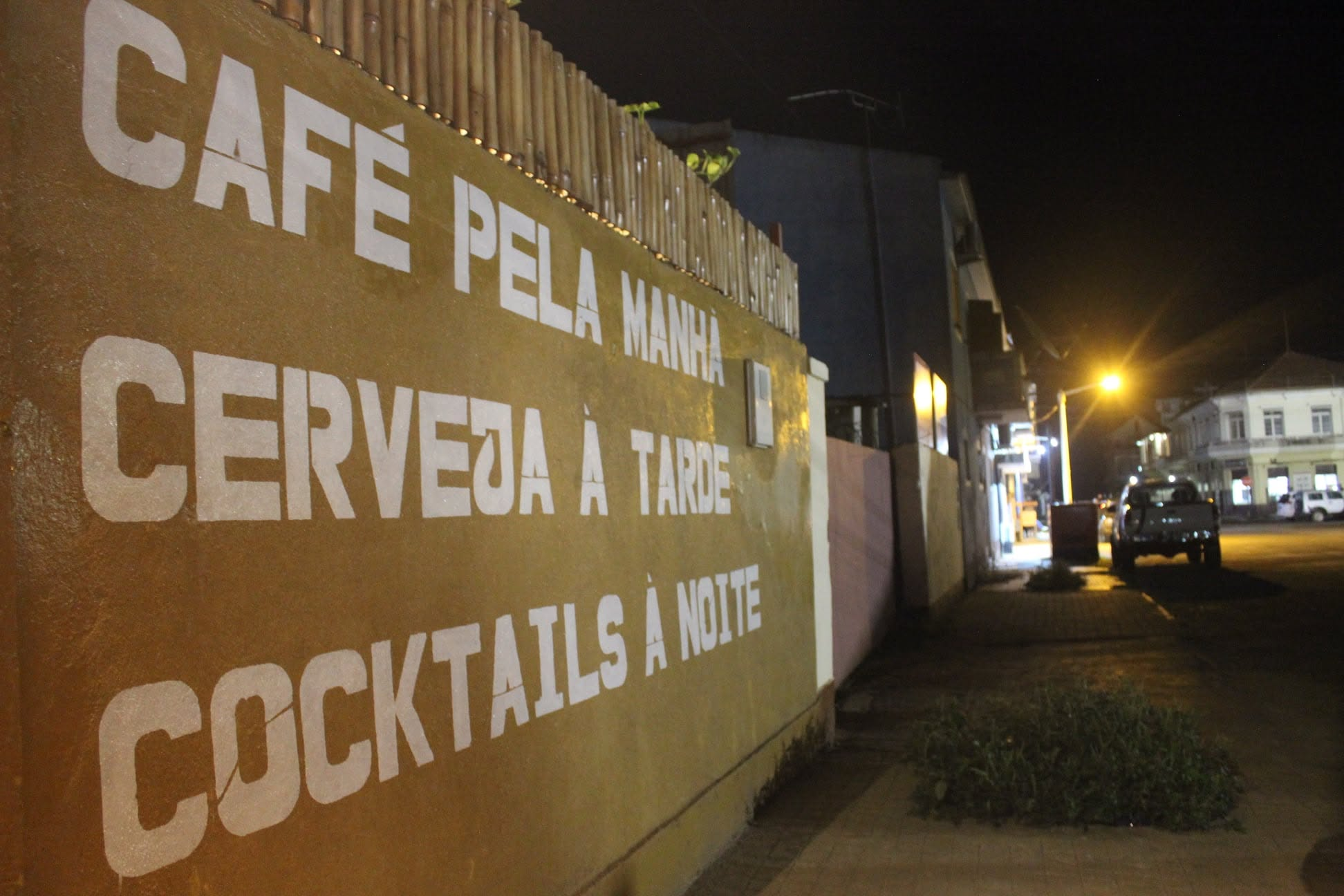 Wall in São Tomé painted with café pela manhã, cerveja à tarde, cocktails à noite, photographed at night
