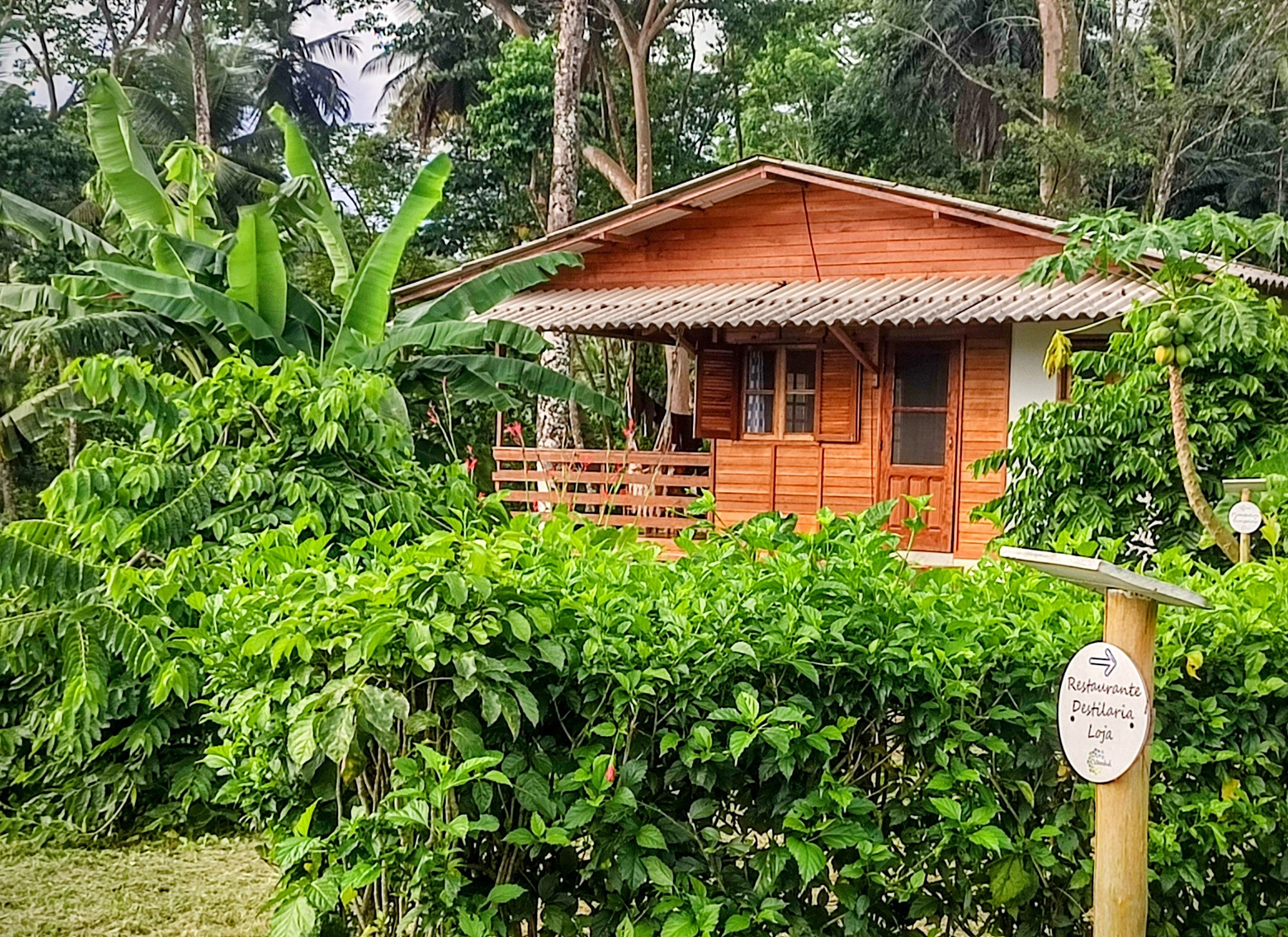 A timber cabin bungalow at the Praia Vanha ecolodge with a signpost pointing to the restaurant and distillery