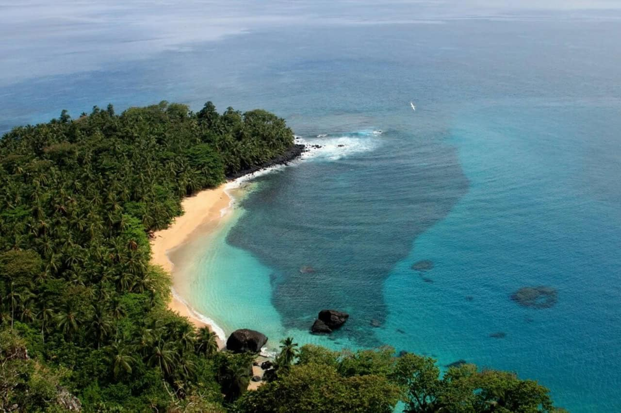 Vista aérea da Praia Banana na ilha do Príncipe, mostrando a curva de areia dourada com floresta de palmeiras e água turquesa