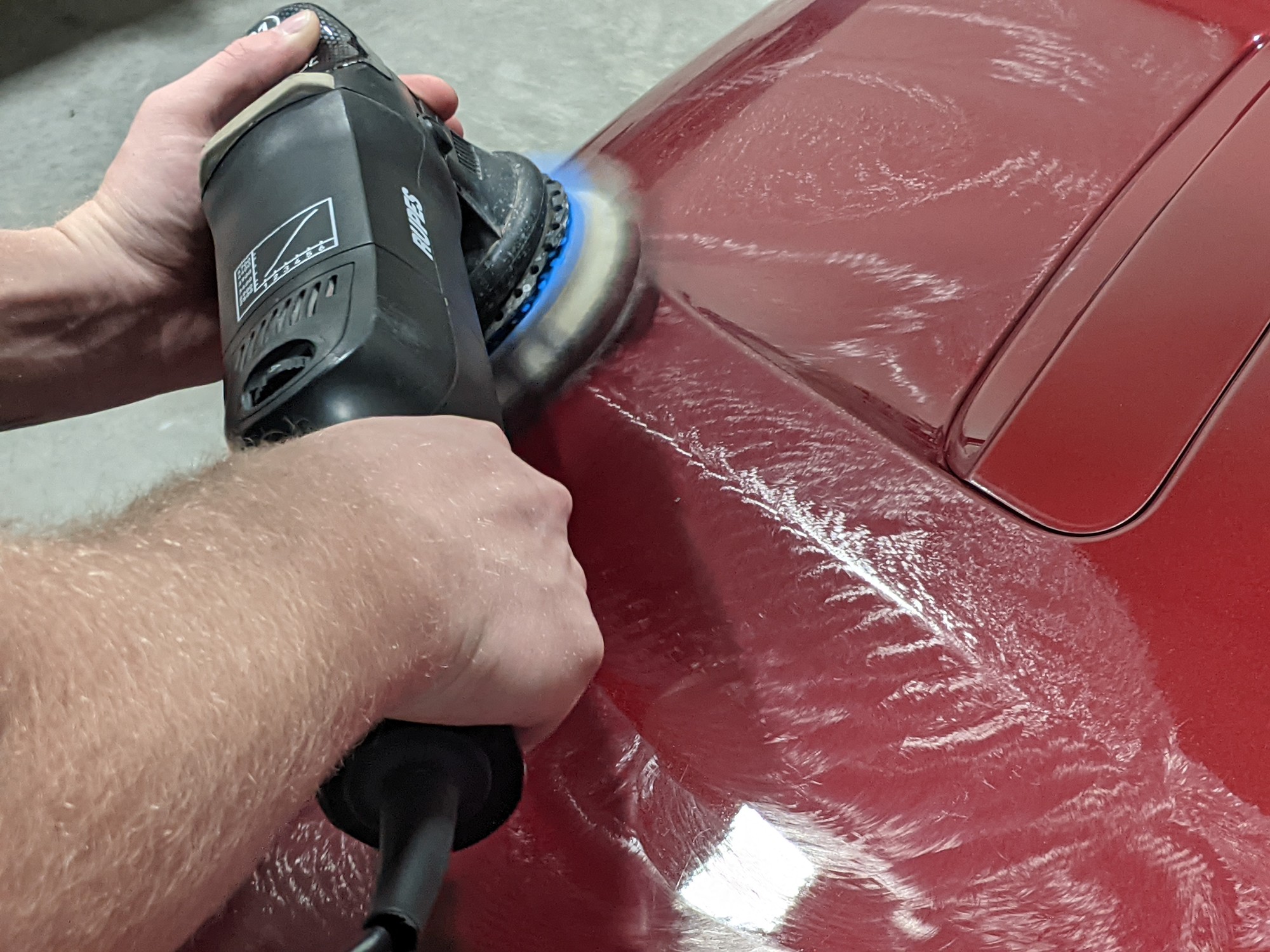 Machine polishing correction work on a red vehicle at Revival Autoworks