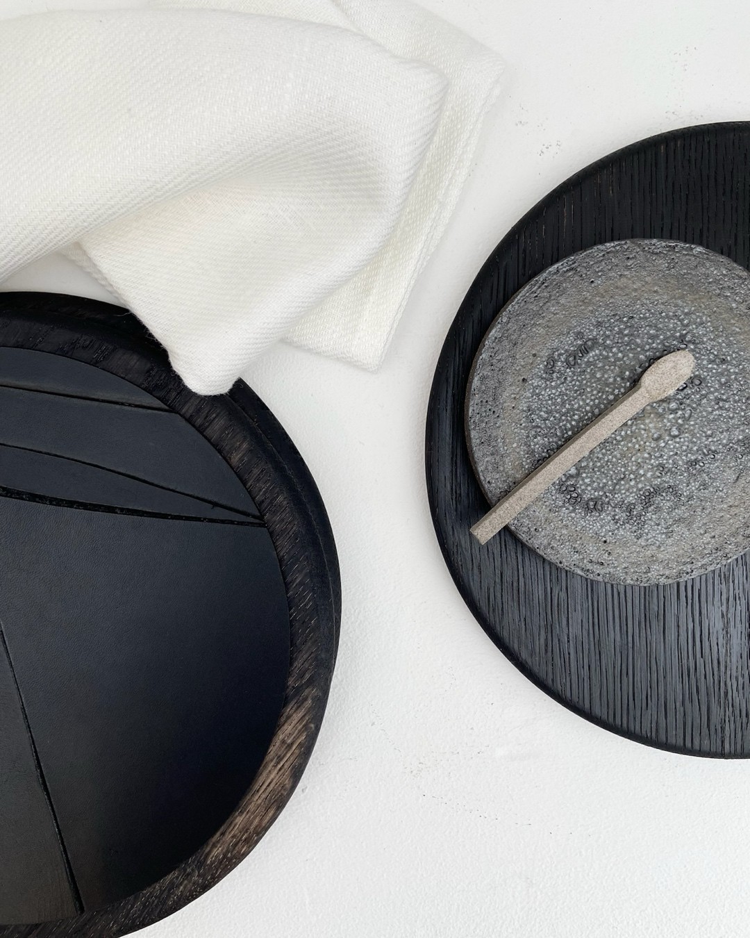 Arrangement of black oak LINFIN underplates with linen and a stone serving dish