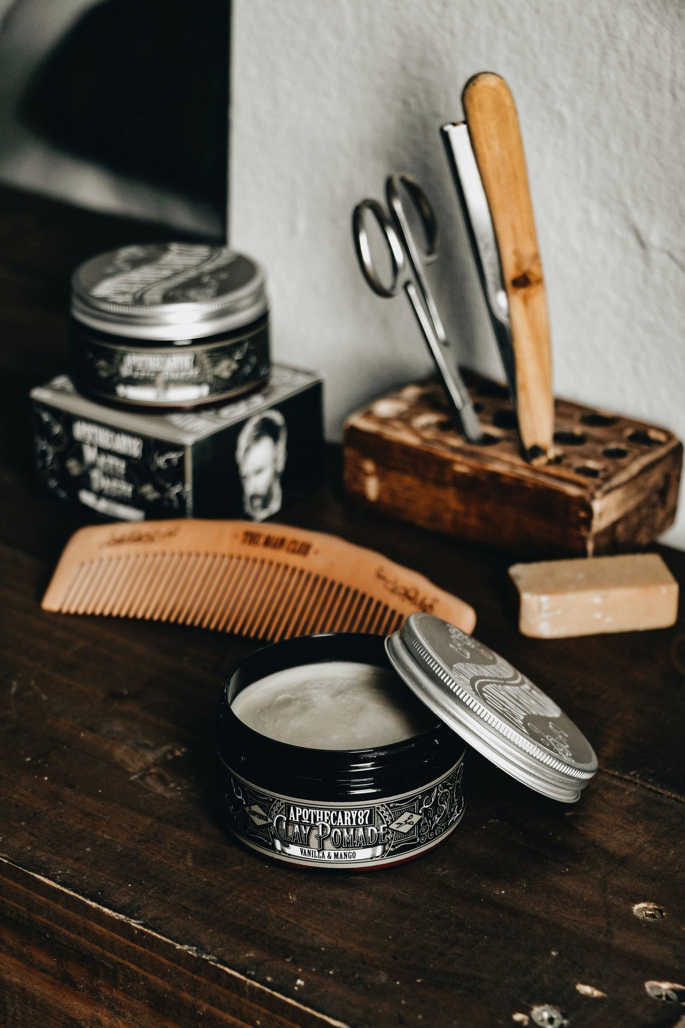 Clay pomade, straight razor, comb and shaving soap on a wooden counter