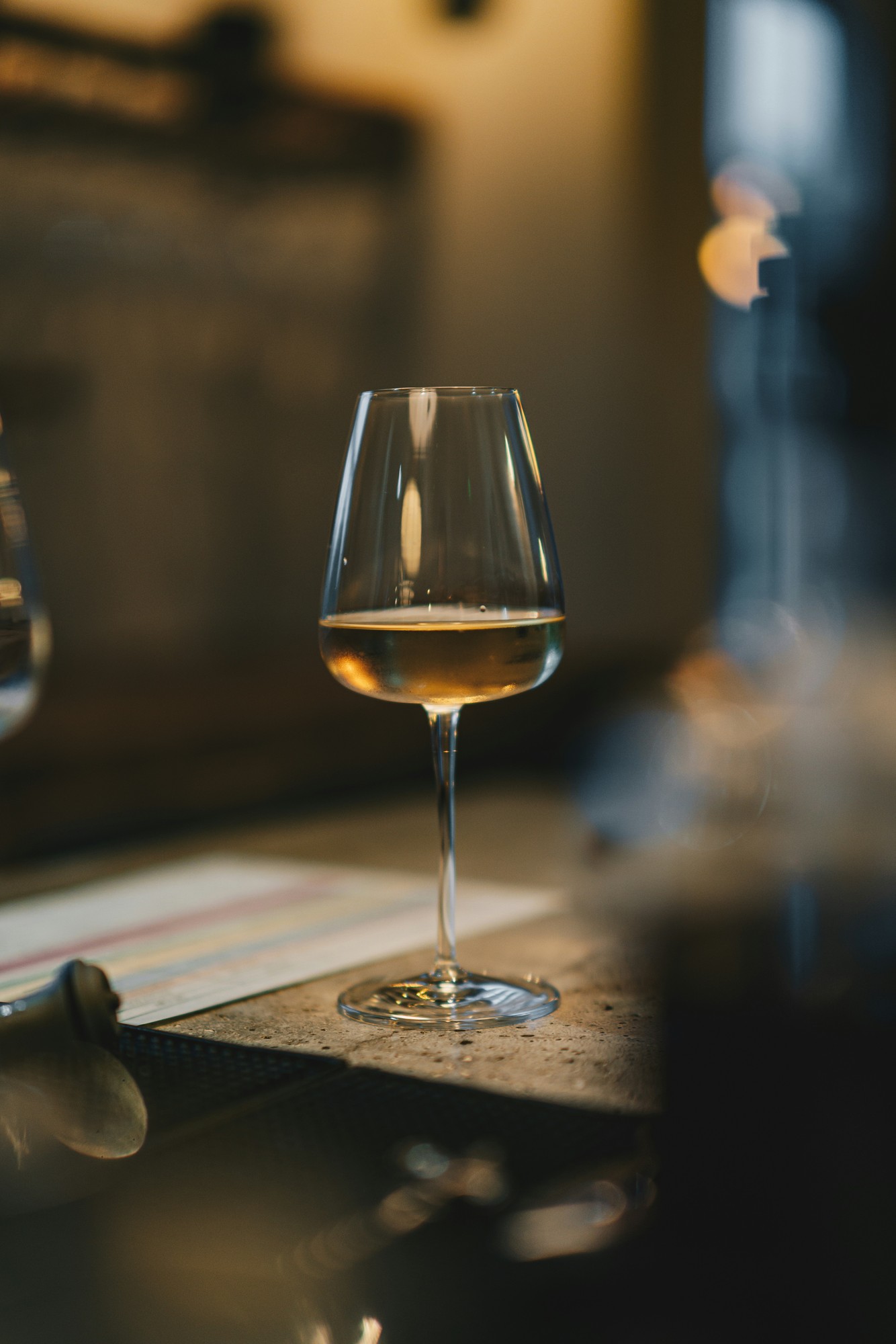 A glass of white wine resting on a bar at dusk