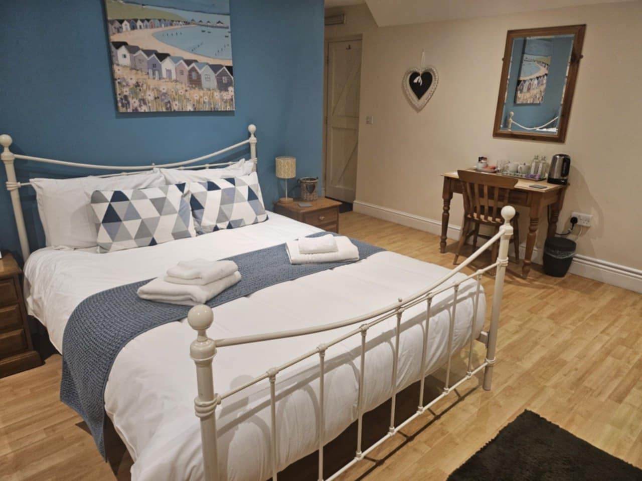 A letting-room bedroom with a white metal bed and coastal artwork at the Eel’s Foot Inn