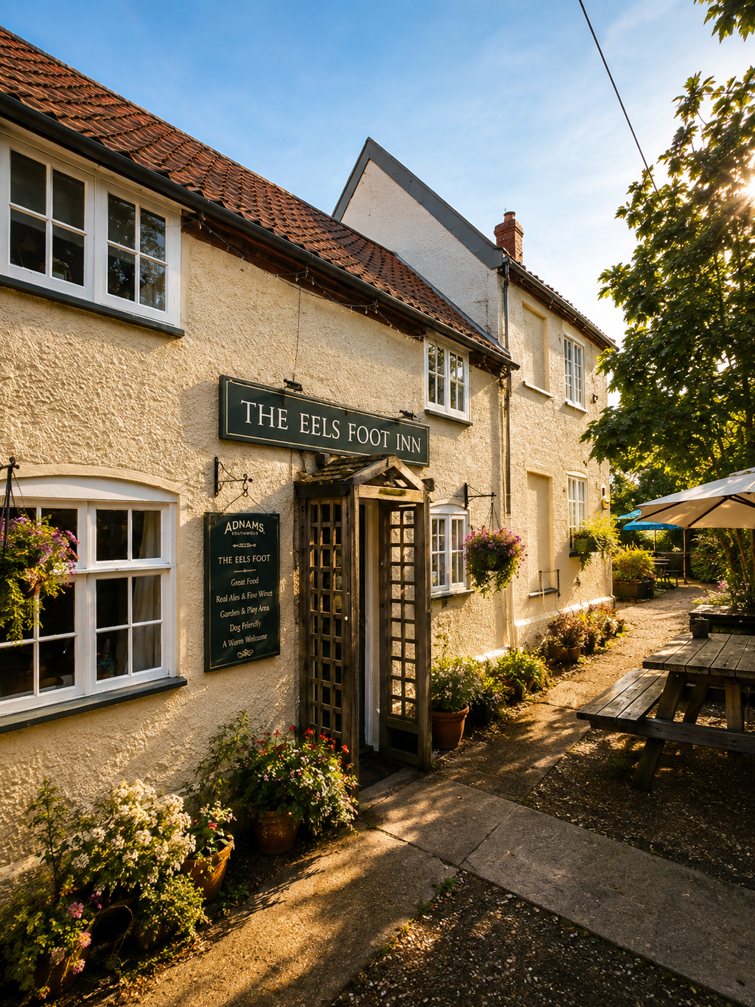 The Eel’s Foot Inn in the evening sun, showing the inn sign, hanging flowers and picnic tables
