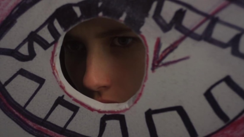 A face peers through a hole cut in a painted wall in Adult World