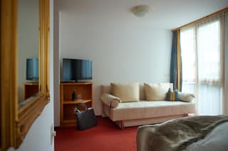 Sitzecke mit Sofa, Fernseher und Balkontür im Doppelzimmer Plus