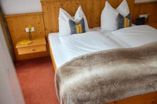 Holzbett mit weißer Bettwäsche und Felldecke im Doppelzimmer Plus