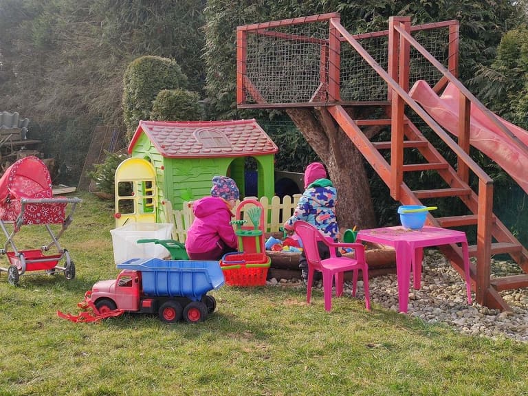 Plac zabaw w ogrodzie z domkiem na drzewie i zjeżdżalnią, plastikowym domkiem, piaskownicą i zabawkami