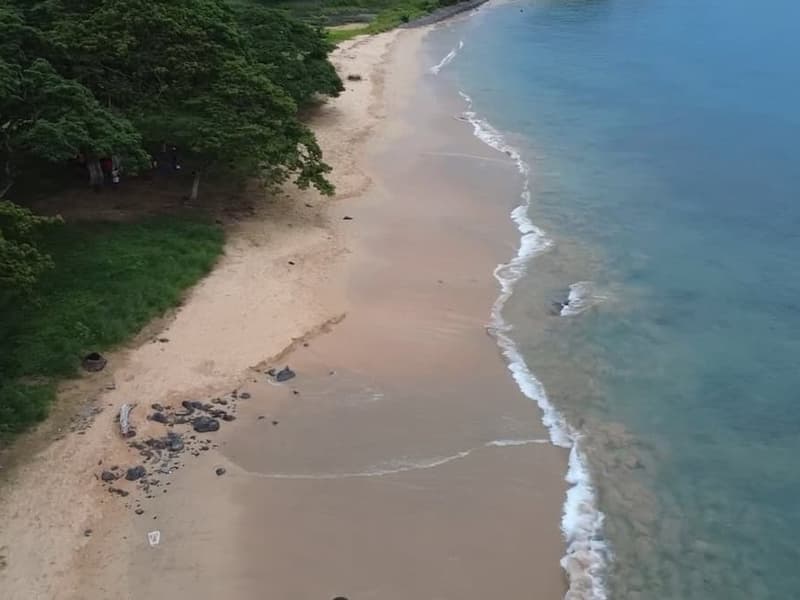 Vista aérea da Praia dos Governadores na costa norte de São Tomé, uma praia larga e tranquila com floresta verde e água calma
