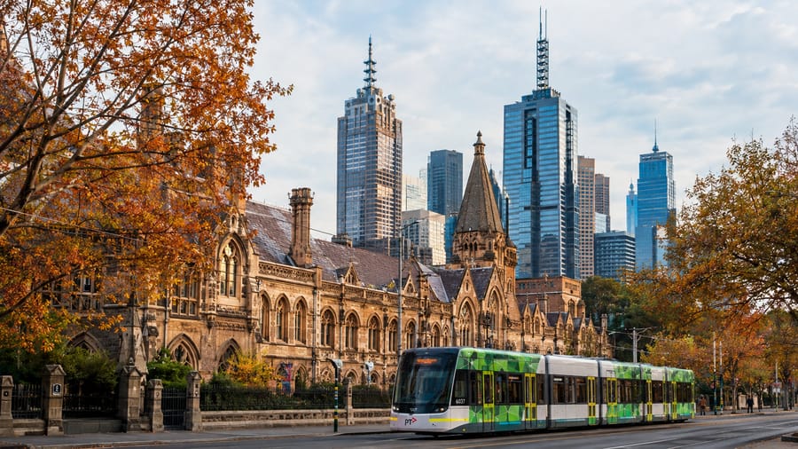 A Melbourne tram passing historic architecture with the city skyline behind