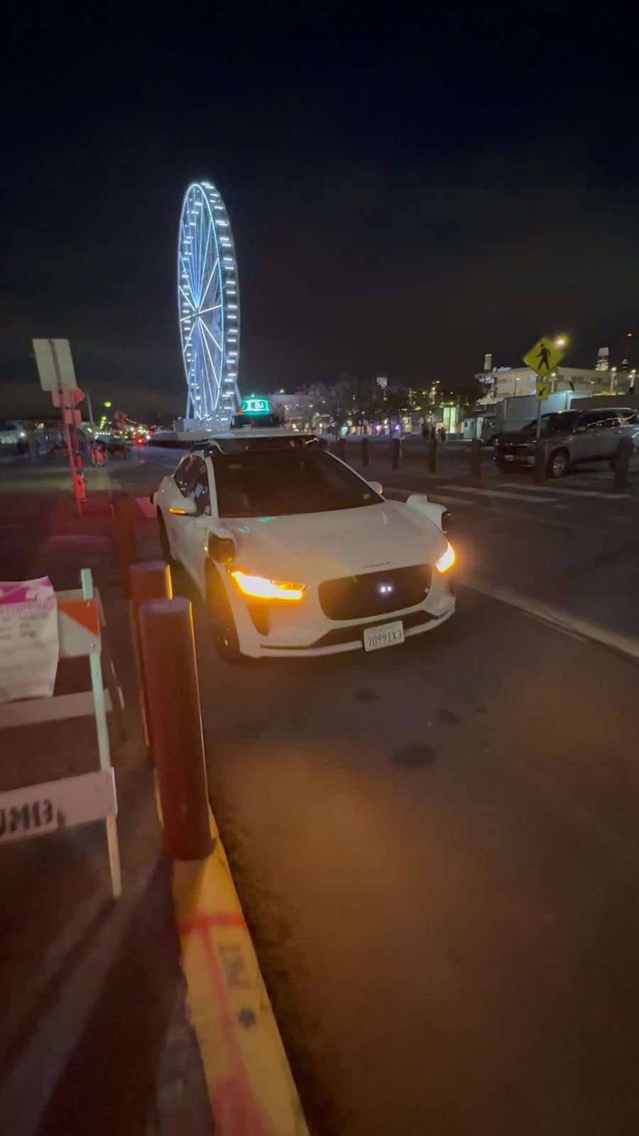 A white Waymo Jaguar I-PACE with its indicator lights on at night in San Francisco