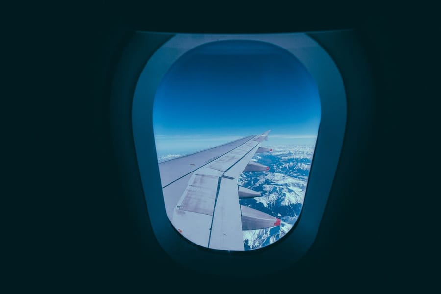Airplane wing over snowy mountains seen through a cabin window