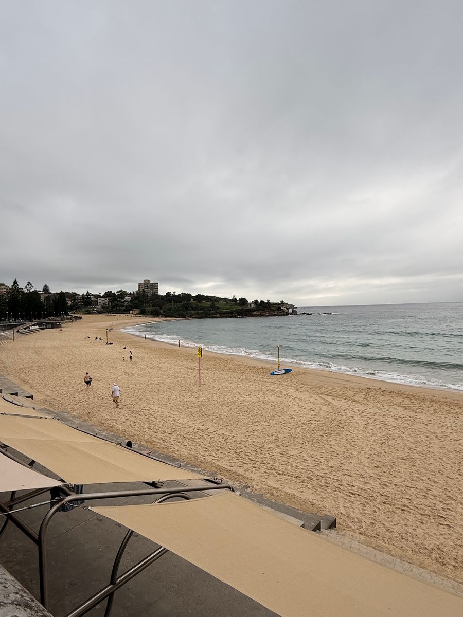 Coogee Beach in Sydney on a cloudy morning, with the promenade and beach umbrellas in the foreground.