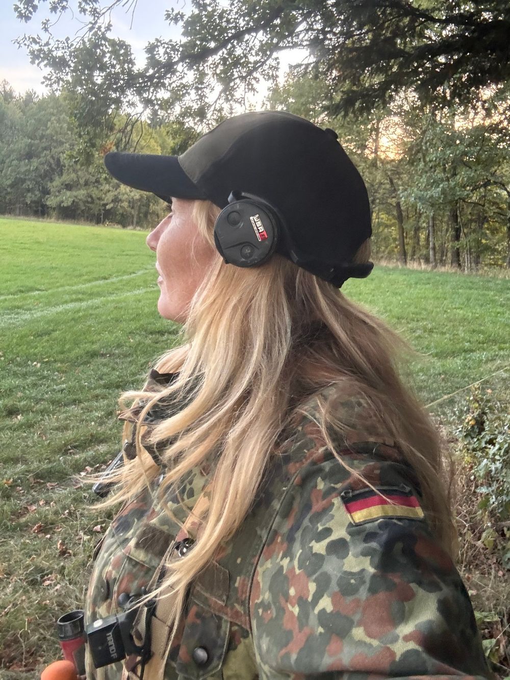 Detector Lady in camouflage and a cap, listening for a signal across an open field