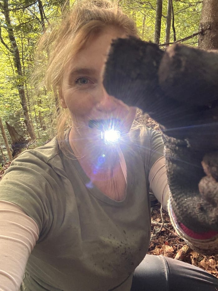 Detector Lady in the woods, headphones on and a muddy glove raised