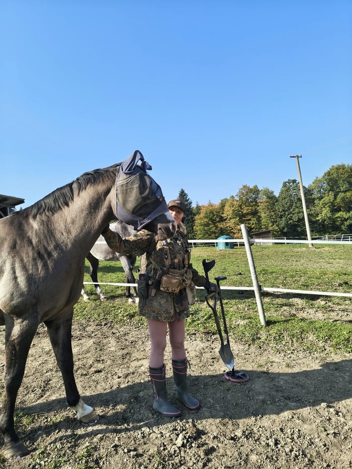 Detector Lady with her detector in a Czech field beside a horse