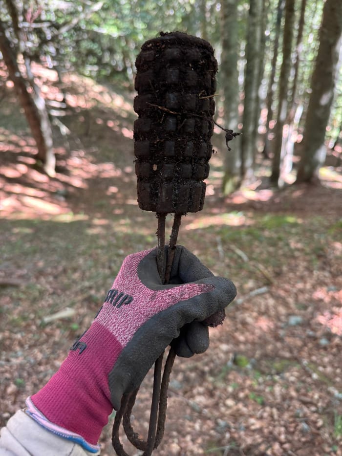 An Austro-Hungarian grenade held up in a gloved hand in woodland