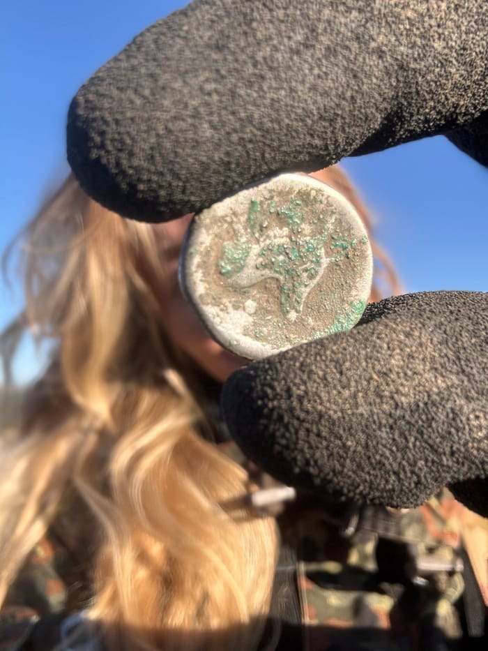 A silver coin held up in a gloved hand, fresh from the soil