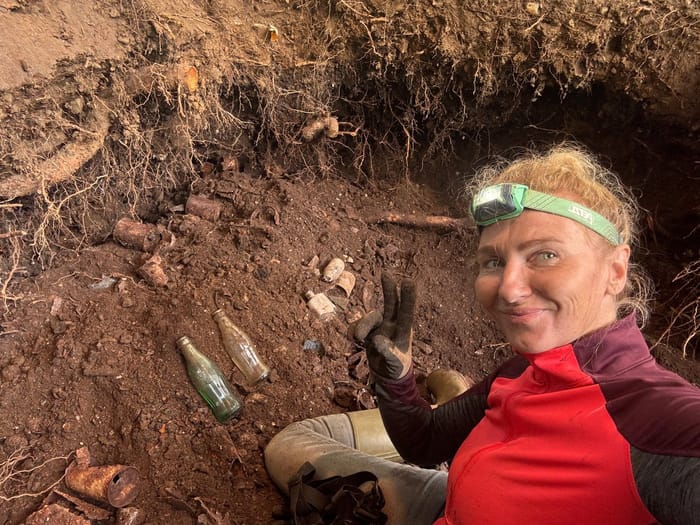 Detector Lady in a dug pit with old bottles and wartime relics around her