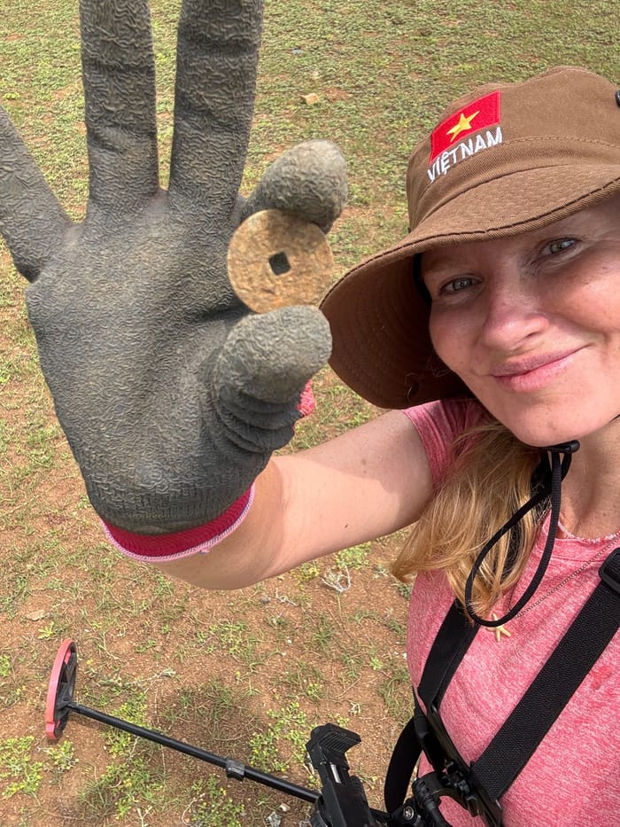 Detector Lady in a Vietnam cap holding a Vietnamese coin she has just found