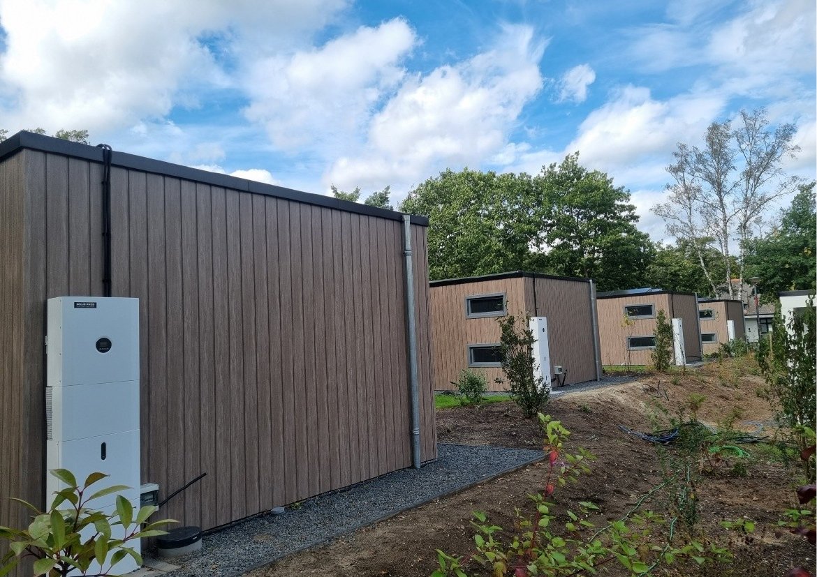 Zes chalets op een park, elk met een eigen thuisbatterij aan de buitenmuur