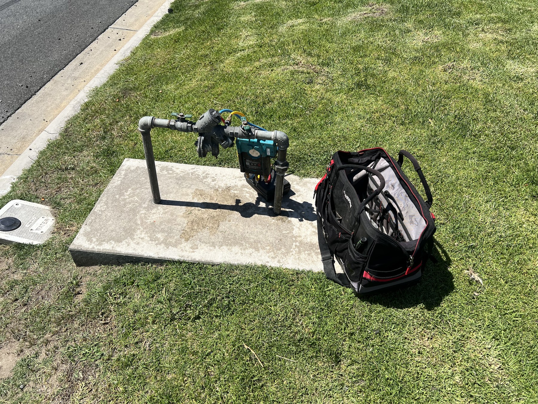 Backflow preventer on a concrete pad in a lawn with certified tester tool bag on site