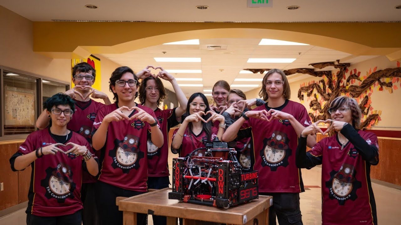 The six members of team 9876 The Countdown making heart shapes with their hands around robot Turbine