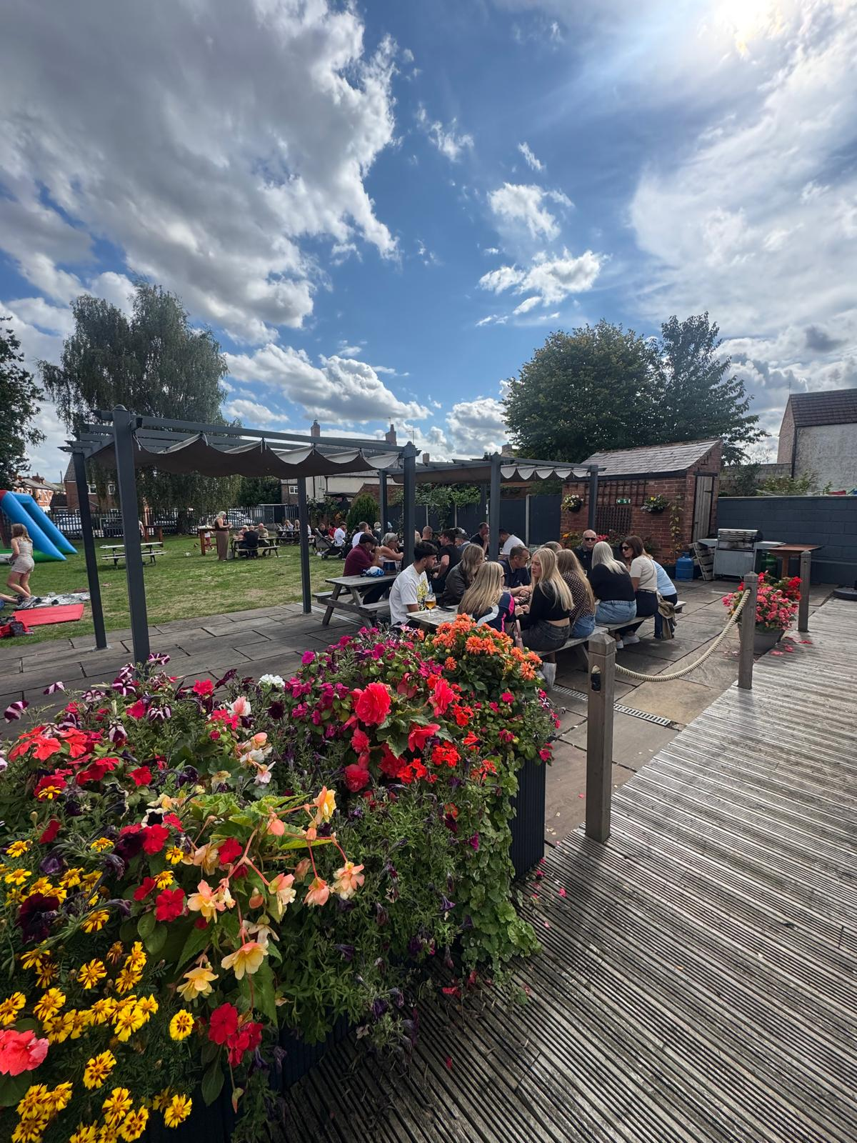 A busy summer day in the beer garden, with tables, planters and pergolas in the sunshine