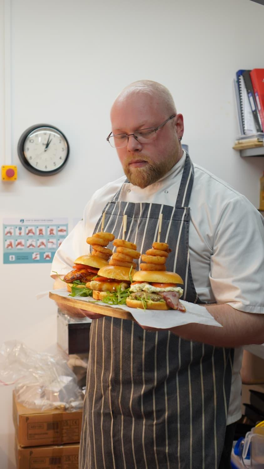 The Star Inn chef carrying a board of stacked burgers with onion rings