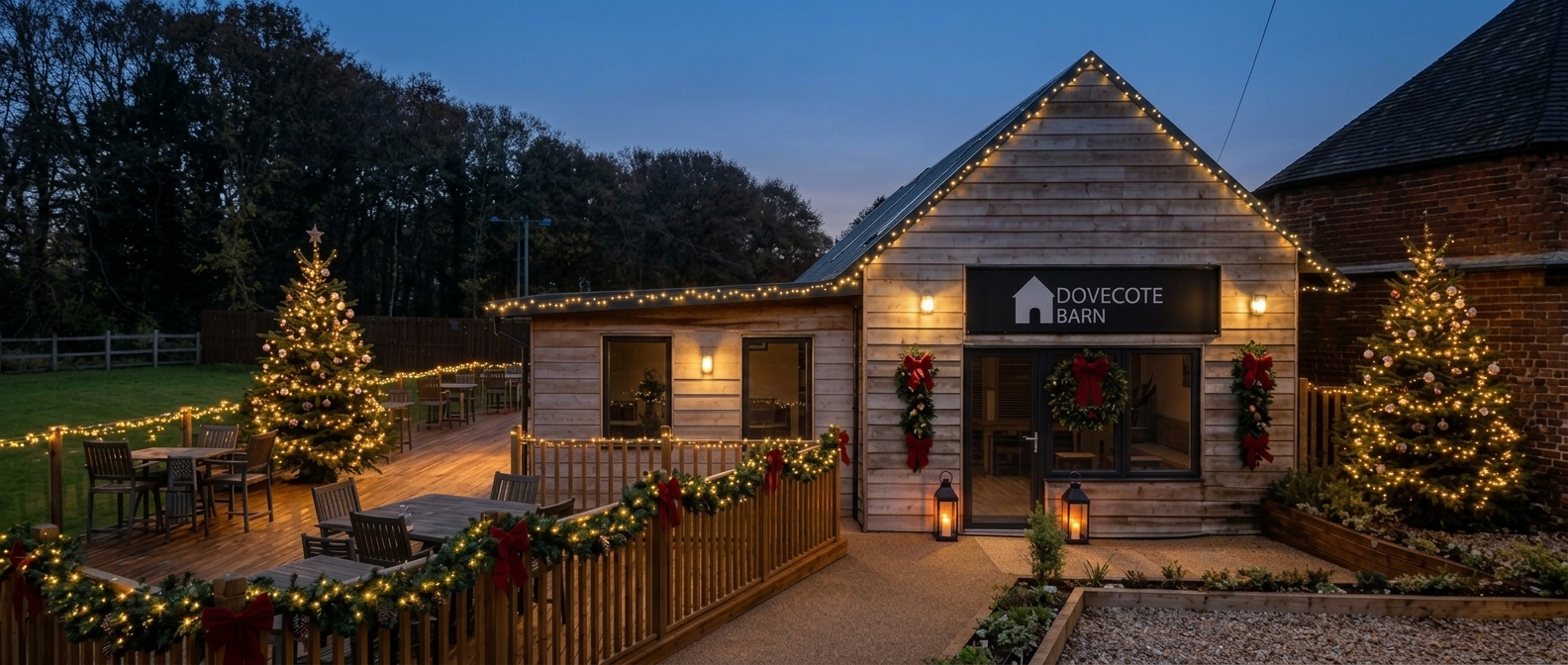The Dovecote Barn decorated for Christmas with a decorated tree on the decking, a wreath on the door, tinsel garlands and fairy lights