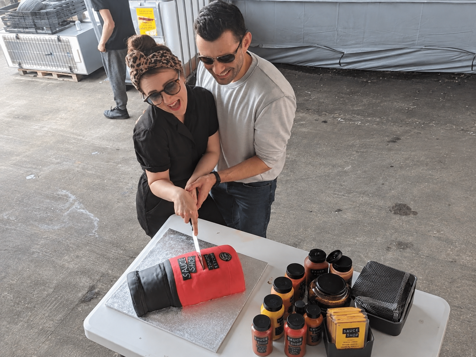 Pam and James cutting a celebration cake surrounded by Sauce Shop bottles