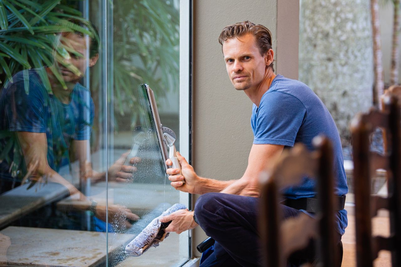 Cleaner in a blue t-shirt washing an office window with a squeegee