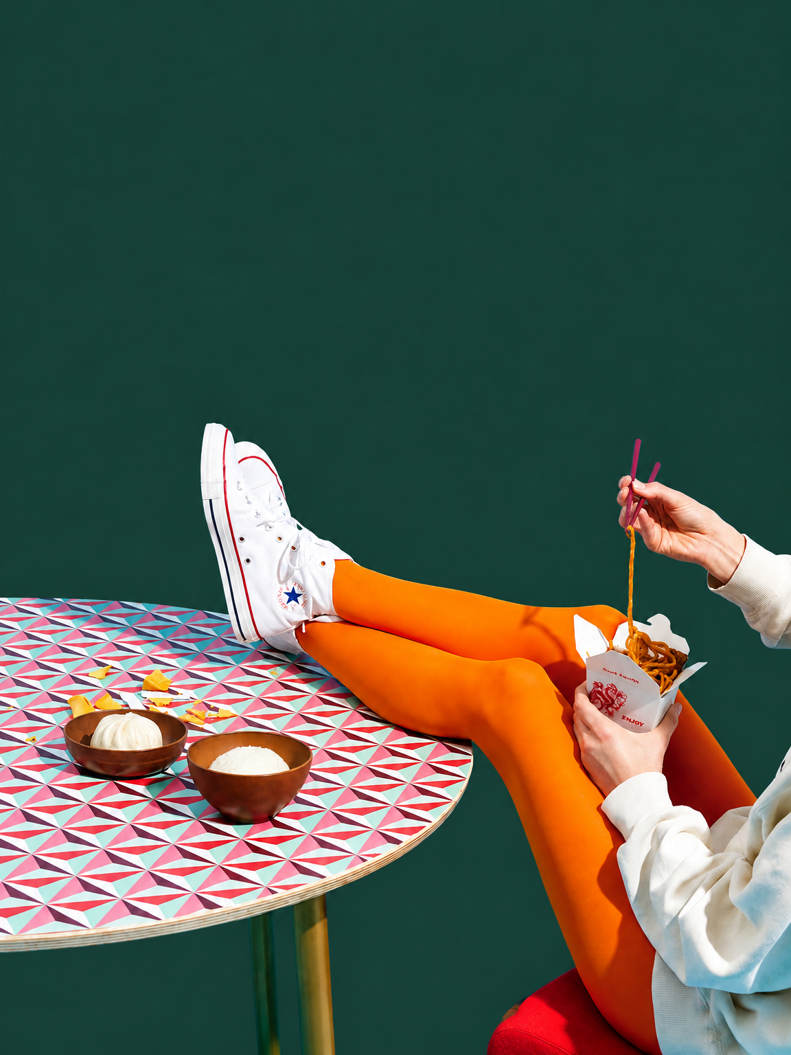 Kim met oranje panty en witte sneakers aan een kleurrijke tafel met noedels