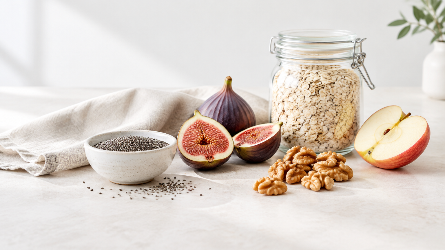 Chia seeds, fresh figs, walnuts, oats and a sliced apple arranged on a pale stone countertop