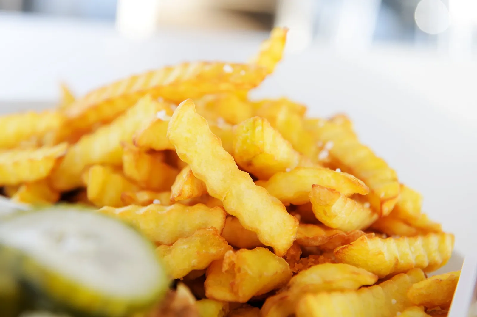 Nærbillede af bølgeskårne pommes frites og en agurkeskive