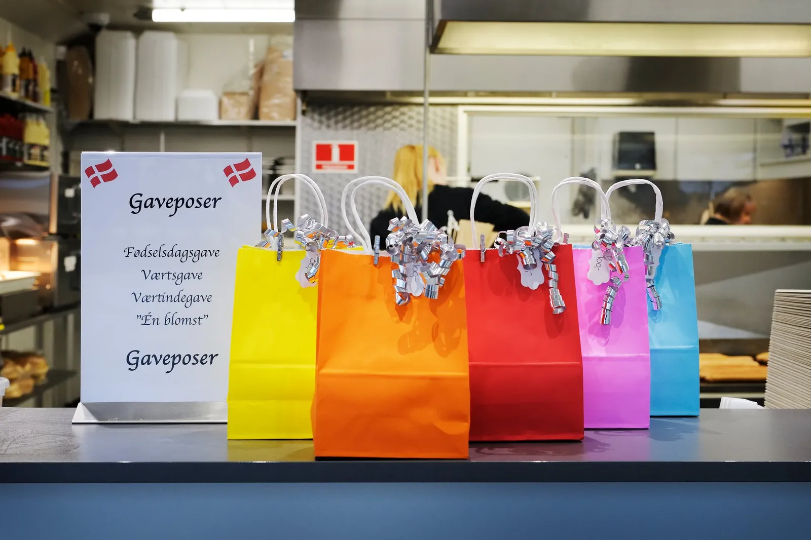 Farverige gaveposer og et skilt med teksten Gaveposer på disken