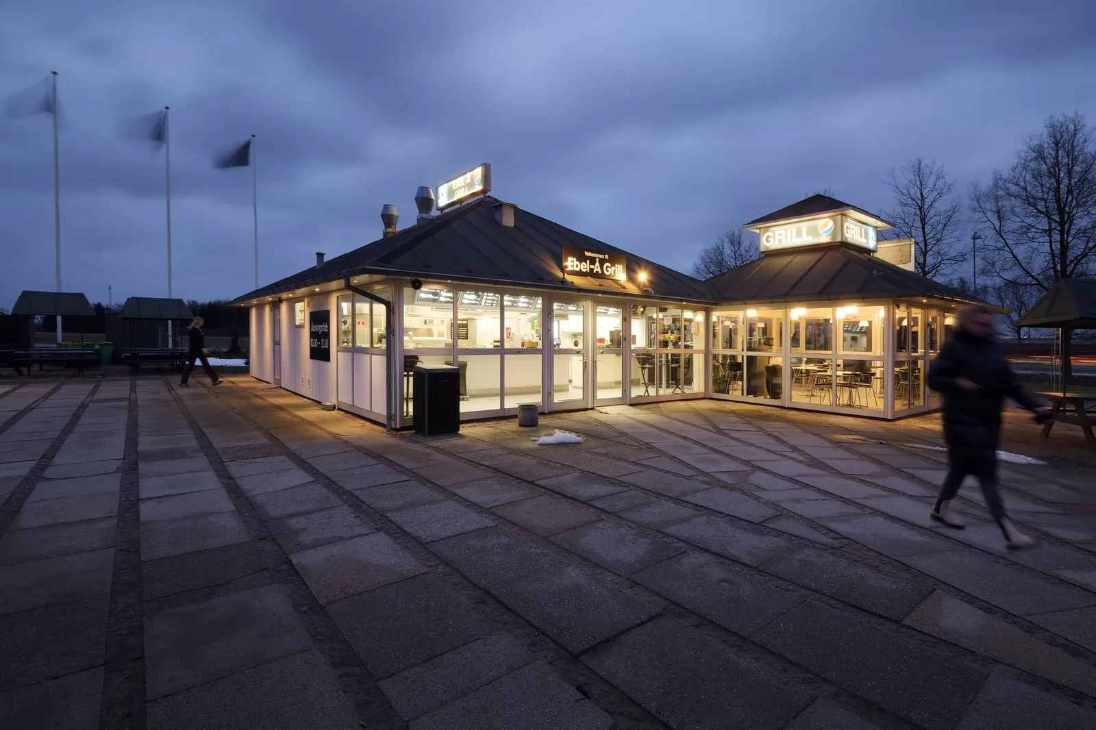 Ebel-Å Grill oplyst om aftenen med flag og en person på pladsen foran