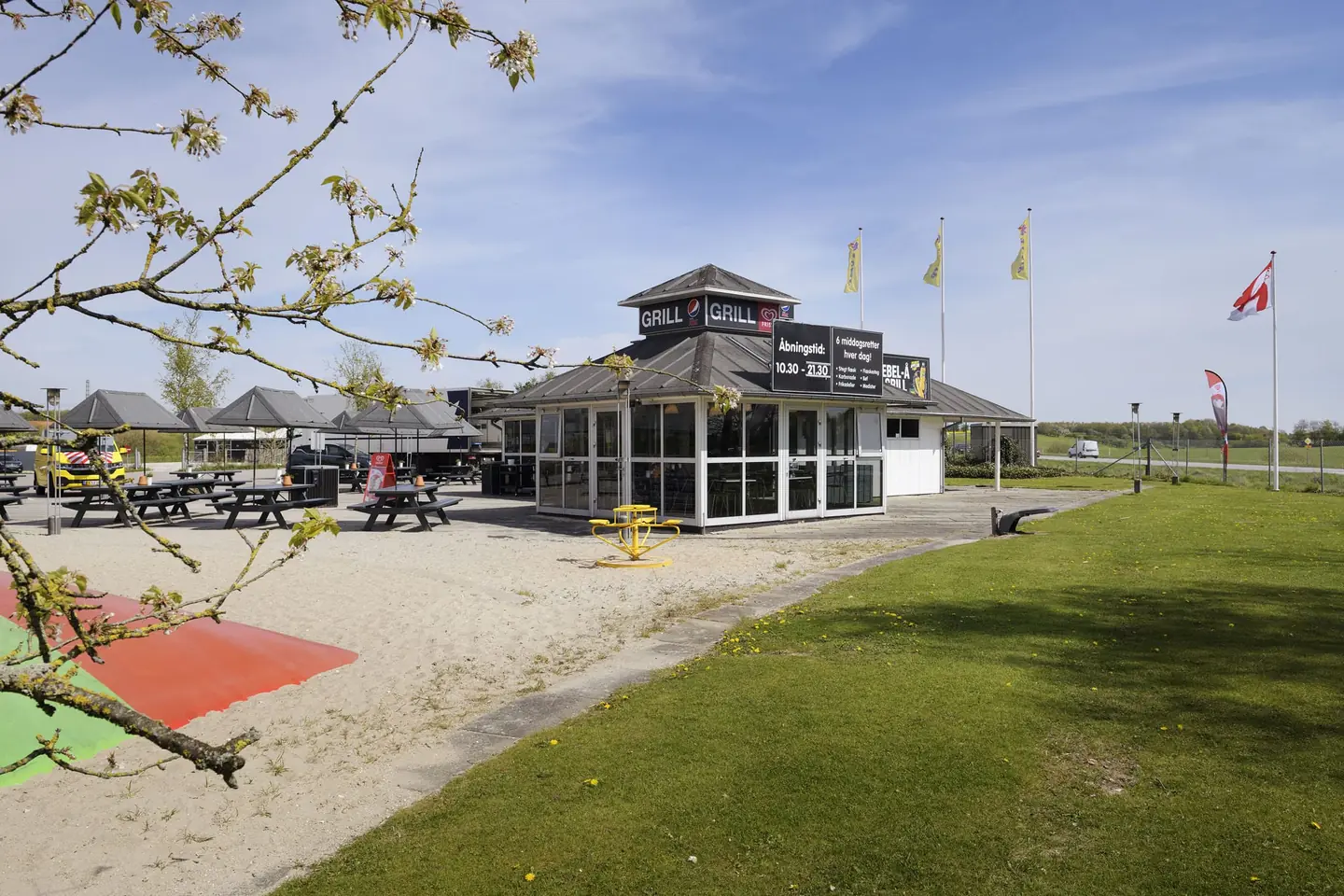 Ebel-Å Grill med flag, picnicborde og græsplæne en solrig dag