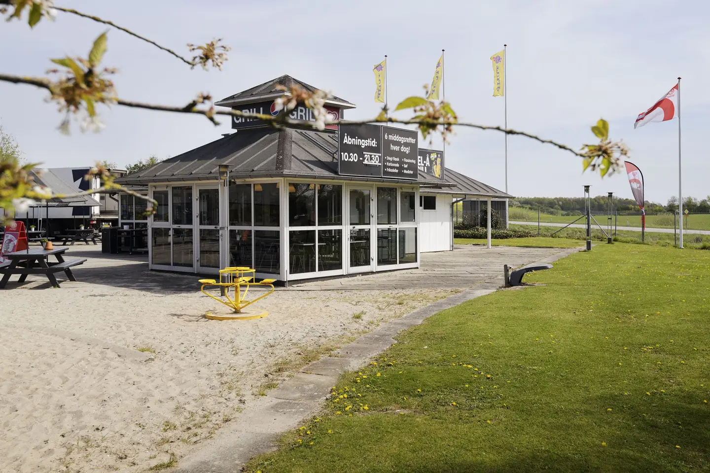 Ebel-Å Grill i solskin med flag, sandplads og græsplæne