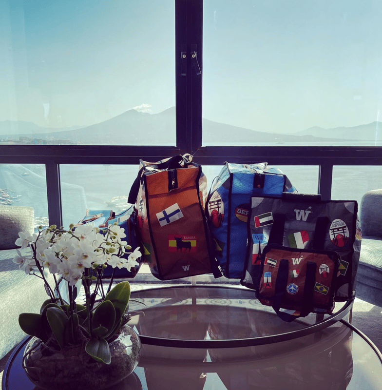 Several WISSHH bags and an orchid on a glass table with a mountain view through the window