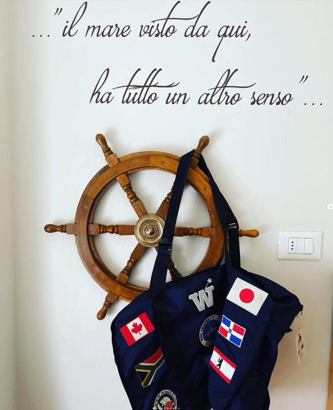 A navy WISSHH bag with international flags hanging from a ship's wheel below an Italian quote