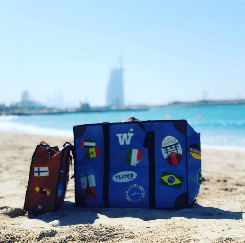 A blue WISSHH Travel Bag and a smaller bag on the sand with the Burj Al Arab skyline behind
